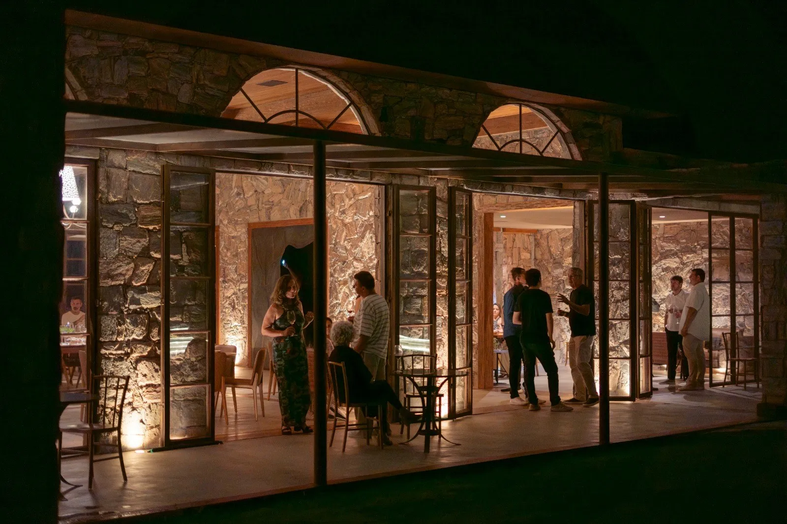 Casa Vinnus iluminada à noite, com convidados no salão de pedra