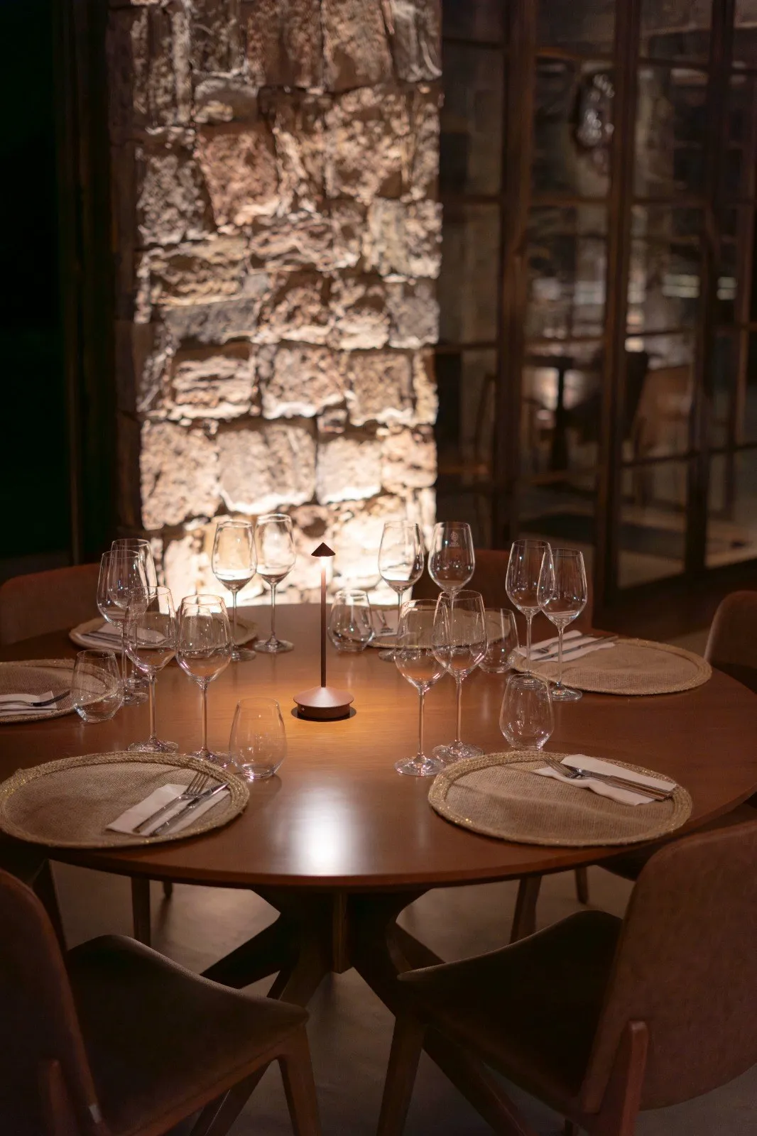 Mesa posta para degustação na Casa Vinnus, com taças e parede de pedra iluminada